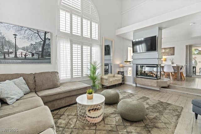 living room featuring a towering ceiling, wood-type flooring, and a multi sided fireplace
