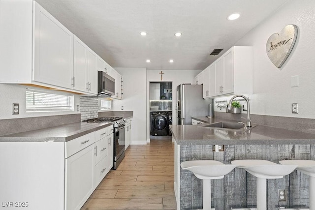 kitchen featuring a breakfast bar, a sink, appliances with stainless steel finishes, washer / clothes dryer, and recessed lighting