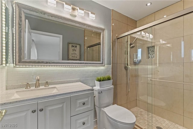 bathroom with toilet, tile walls, a shower stall, decorative backsplash, and vanity