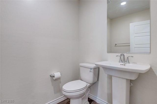 half bath with toilet, baseboards, and wood finished floors