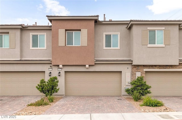 townhome / multi-family property featuring an attached garage, decorative driveway, and stucco siding