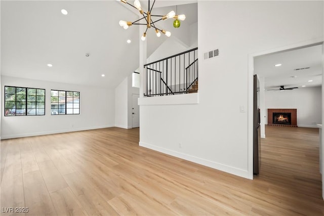 unfurnished living room featuring light wood finished floors, visible vents, baseboards, and high vaulted ceiling