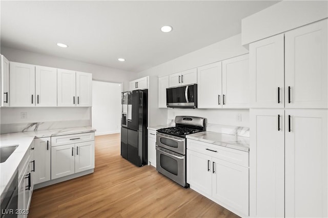 kitchen featuring light wood-type flooring, light stone countertops, white cabinetry, and black appliances