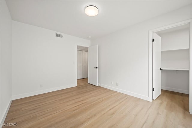 unfurnished bedroom with light wood-style flooring, a closet, visible vents, baseboards, and a spacious closet