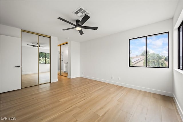 unfurnished bedroom with light wood-style flooring, a ceiling fan, multiple closets, visible vents, and baseboards