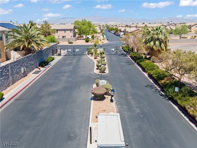 view of asphalt street featuring curbs, a gated entry, and a residential view