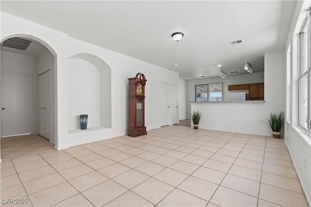 unfurnished living room with light tile patterned flooring and arched walkways