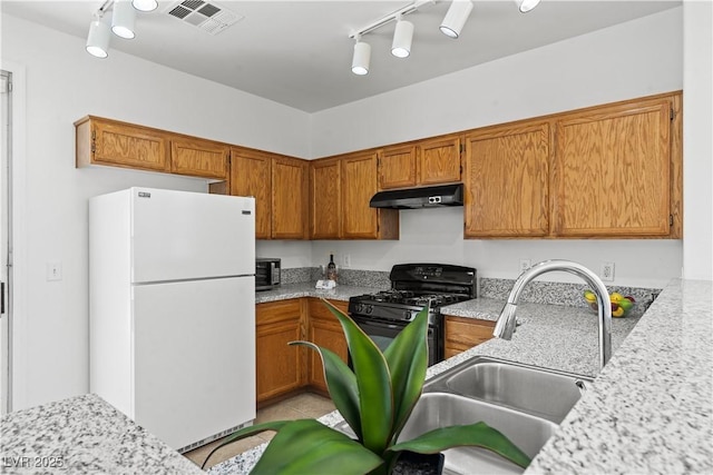 kitchen with freestanding refrigerator, rail lighting, under cabinet range hood, a sink, and black gas stove
