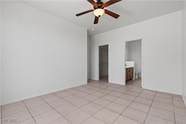unfurnished bedroom featuring a spacious closet, light tile patterned flooring, a closet, ensuite bathroom, and a ceiling fan