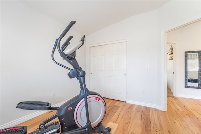 exercise room with light wood-style floors, vaulted ceiling, and baseboards
