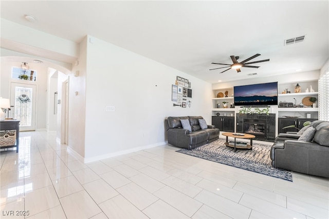 living area featuring visible vents, baseboards, ceiling fan, arched walkways, and built in shelves
