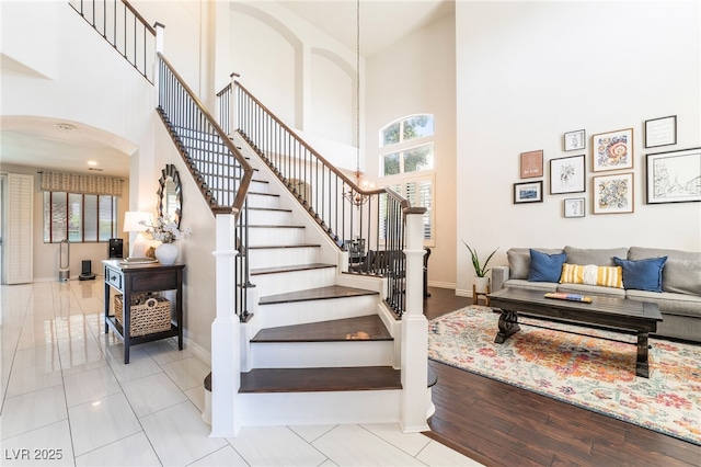 stairway with arched walkways, plenty of natural light, and a high ceiling