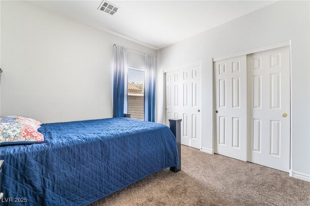 bedroom with two closets, visible vents, baseboards, and carpet floors