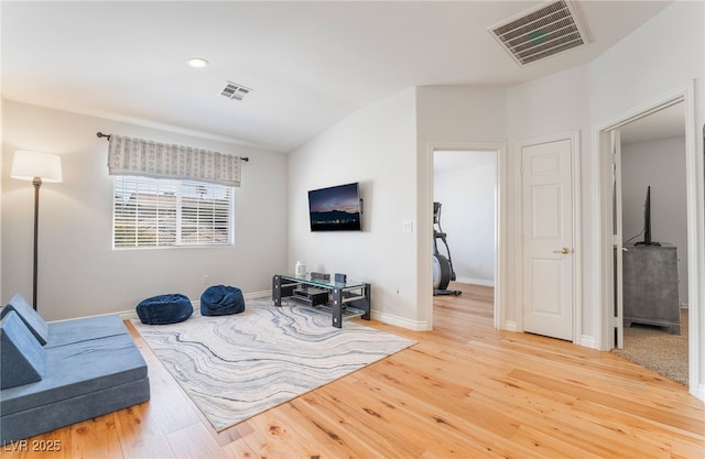 living area with vaulted ceiling, visible vents, and light wood-style floors