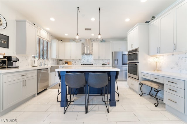 kitchen with wall chimney range hood, decorative backsplash, a breakfast bar area, and appliances with stainless steel finishes