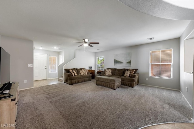 living room featuring baseboards, carpet flooring, visible vents, and a ceiling fan