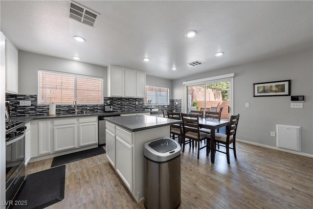 kitchen with stainless steel dishwasher, backsplash, dark countertops, and visible vents