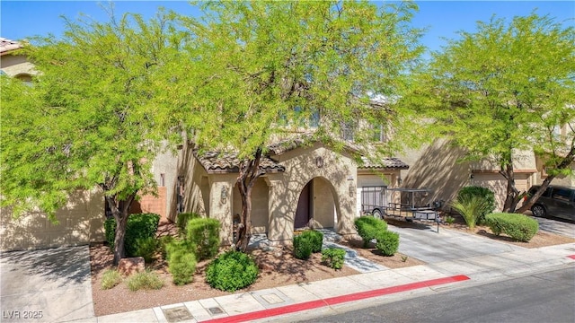 mediterranean / spanish-style home with a tile roof, a garage, stucco siding, and driveway