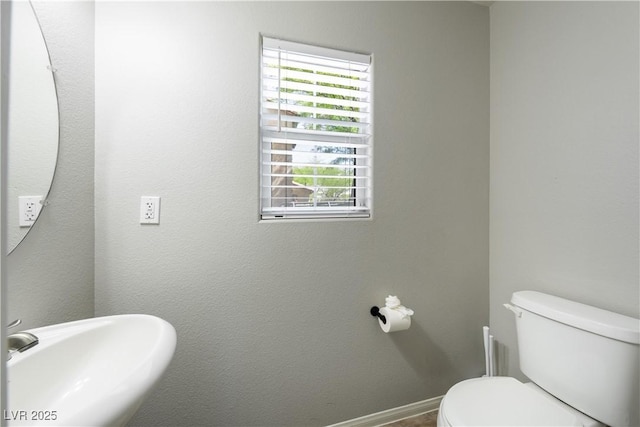 half bath featuring a sink, toilet, and baseboards