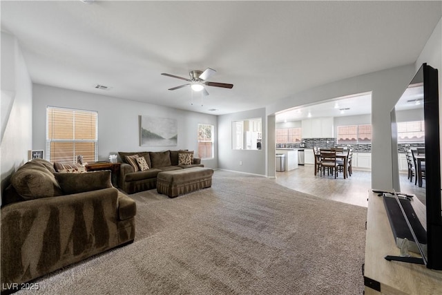 living area featuring visible vents, baseboards, ceiling fan, arched walkways, and light carpet