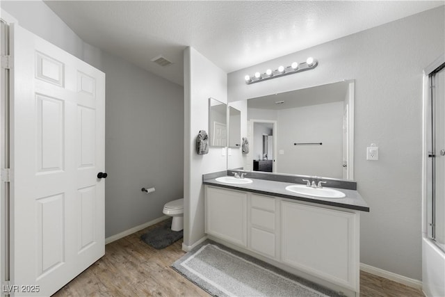 bathroom with double vanity, toilet, wood finished floors, a sink, and visible vents