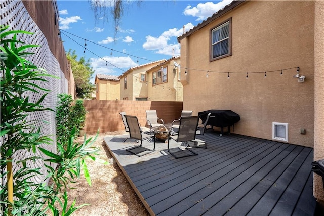 wooden deck with area for grilling, a fire pit, and fence