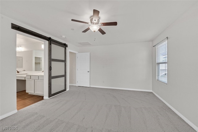 2486 Dragon Fire Ln, Henderson, NV 89052 - unfurnished bedroom featuring ensuite bath, a barn door, carpet floors, a ceiling fan, and baseboards