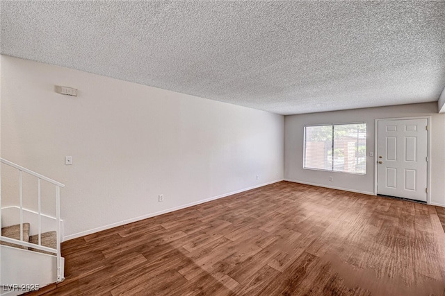 unfurnished living room with baseboards, stairs, a textured ceiling, and wood finished floors