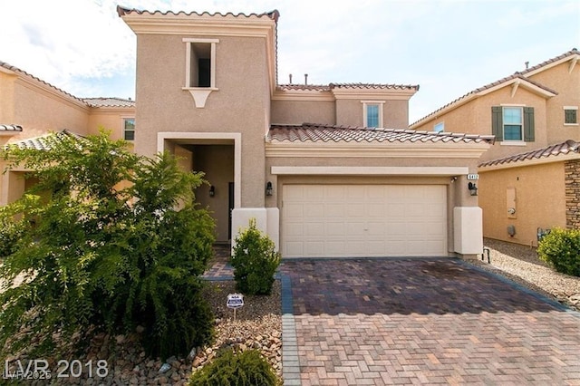 mediterranean / spanish house with stucco siding, a tiled roof, a garage, and decorative driveway