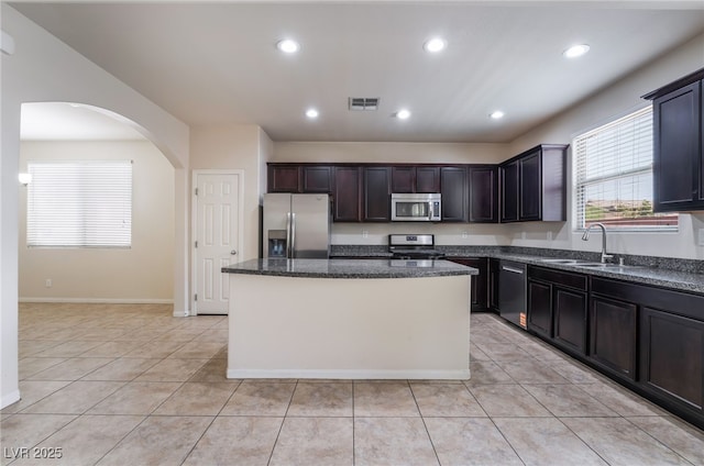 6412 Dimatteo St, Las Vegas, NV 89148 - kitchen featuring appliances with stainless steel finishes, a kitchen island, arched walkways, light tile patterned floors, and dark stone countertops