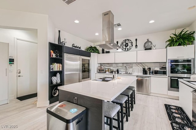 10408 Mezzanino Ct, Las Vegas, NV 89135 - kitchen with light wood finished floors, white cabinetry, stainless steel appliances, and island range hood