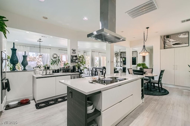 10408 Mezzanino Ct, Las Vegas, NV 89135 - kitchen featuring light wood finished floors, a center island, island exhaust hood, white cabinetry, and visible vents
