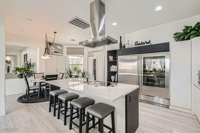 10408 Mezzanino Ct, Las Vegas, NV 89135 - kitchen with black electric cooktop, light wood finished floors, island exhaust hood, and built in fridge