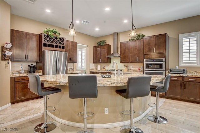 2425 Amatrice St, Henderson, NV 89044 - kitchen with an island with sink, a breakfast bar, stainless steel appliances, visible vents, and wall chimney range hood