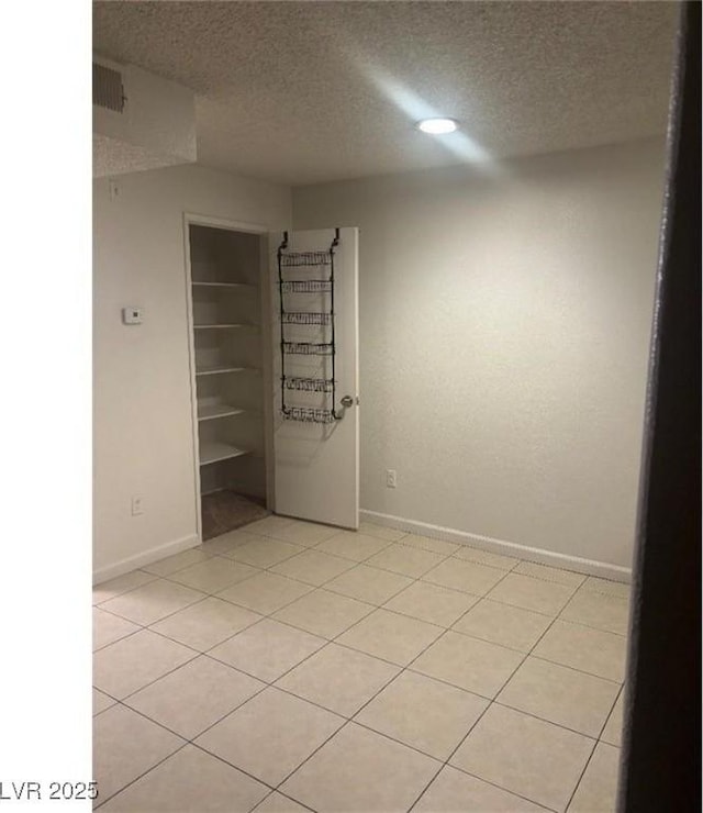 spare room with a textured ceiling, baseboards, and light tile patterned floors