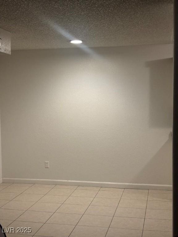 empty room featuring light tile patterned floors, baseboards, and a textured ceiling