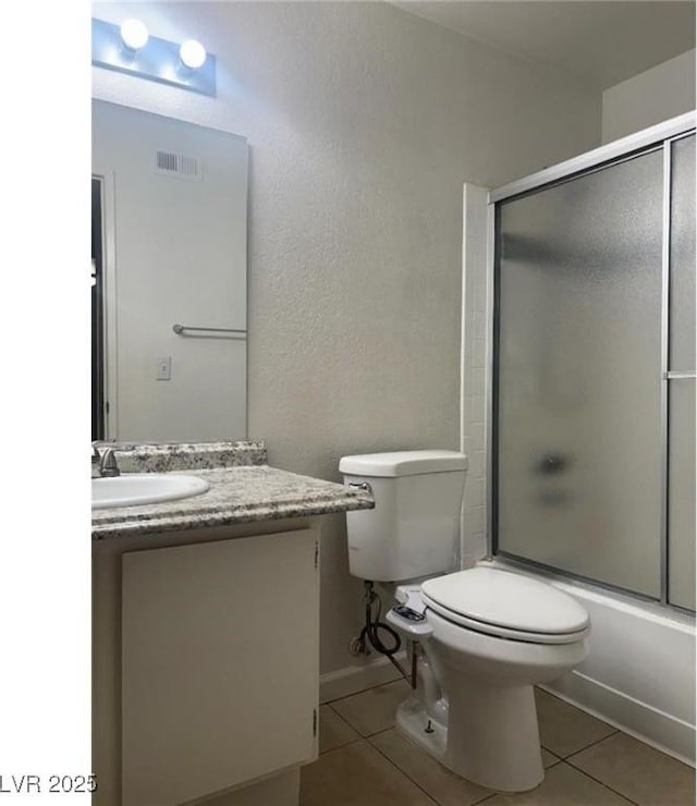 bathroom with toilet, vanity, visible vents, tile patterned flooring, and bath / shower combo with glass door