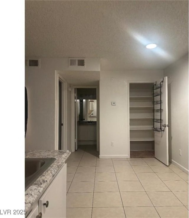 unfurnished bedroom with a textured ceiling, baseboards, light tile patterned floors, and visible vents