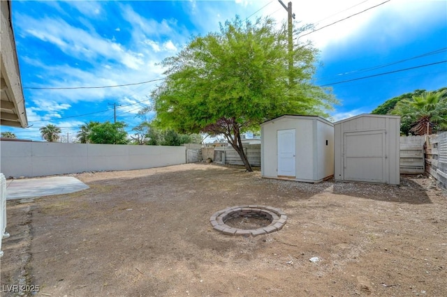 fenced backyard featuring a storage unit, an outbuilding, and an outdoor fire pit