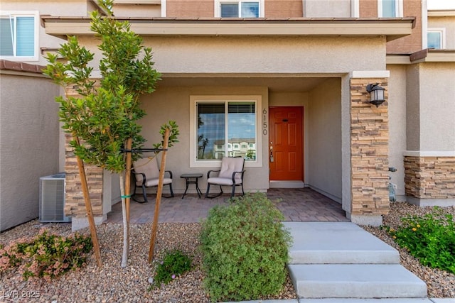 doorway to property featuring central AC unit, stone siding, a porch, and stucco siding