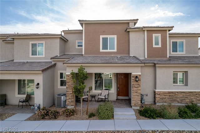 view of front of property featuring cooling unit, covered porch, stucco siding, and stone siding