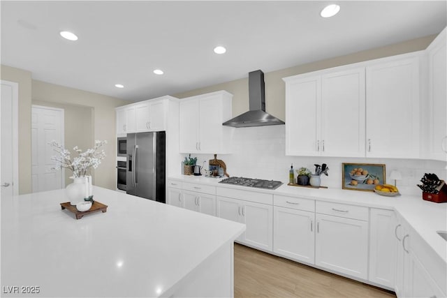 kitchen featuring backsplash, wall chimney range hood, light countertops, white cabinets, and appliances with stainless steel finishes