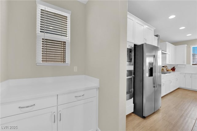 kitchen with stainless steel appliances, recessed lighting, wall chimney exhaust hood, light countertops, and white cabinets