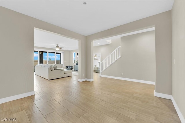 unfurnished living room featuring light wood-type flooring, stairs, baseboards, and a ceiling fan