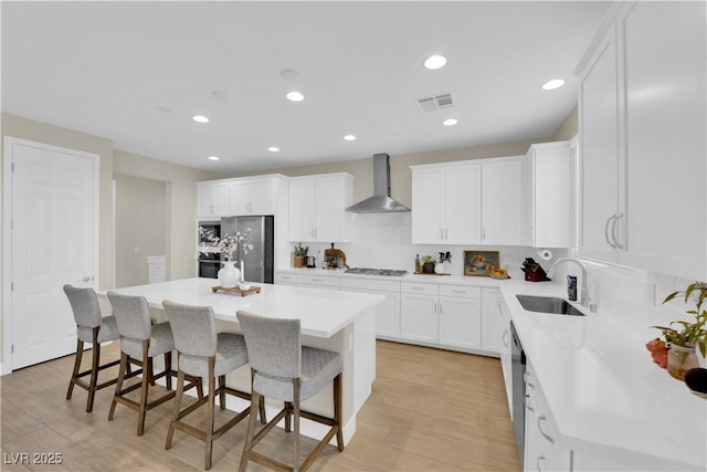 kitchen with a sink, a breakfast bar, visible vents, wall chimney exhaust hood, and appliances with stainless steel finishes