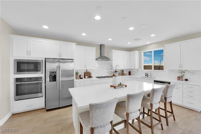 kitchen with wall chimney range hood, a kitchen bar, a center island, white cabinets, and appliances with stainless steel finishes