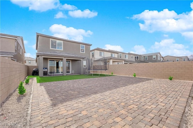rear view of house featuring a trampoline, a residential view, a patio, stucco siding, and a fenced backyard