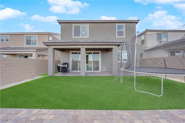 back of house with a lawn, a trampoline, a patio area, stucco siding, and a fenced backyard