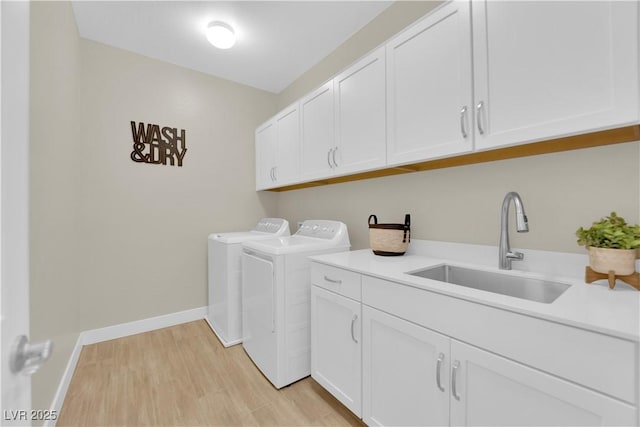clothes washing area with a sink, cabinet space, washing machine and clothes dryer, light wood finished floors, and baseboards