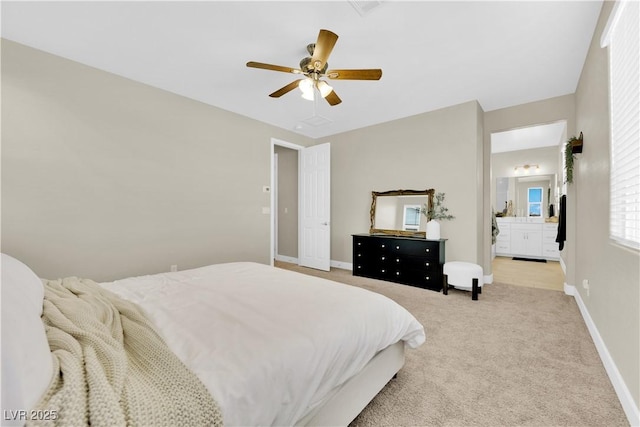bedroom featuring ensuite bath, light carpet, baseboards, and a ceiling fan